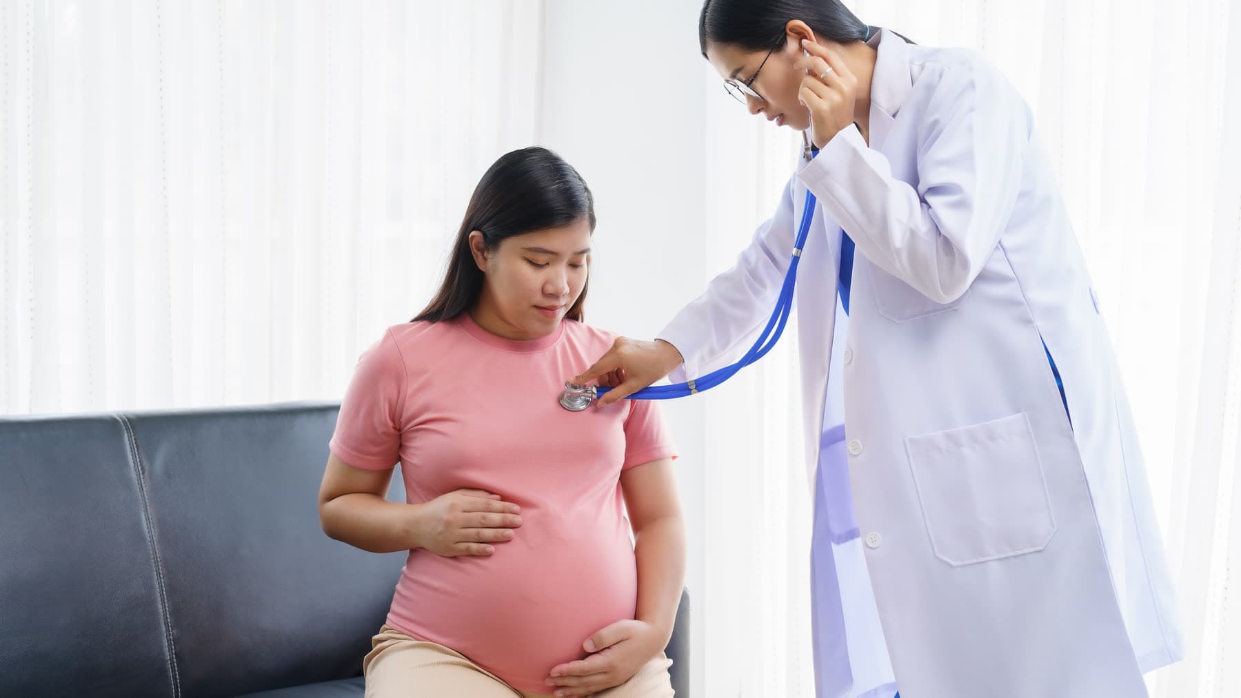 A doctor listens to a pregnant woman’s abdomen with a stethoscope at a check-up