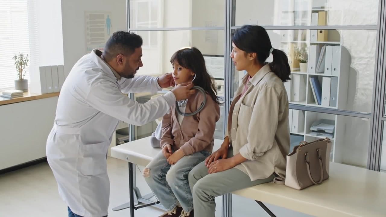A doctor examines a girl sitting beside her mother on the exam table