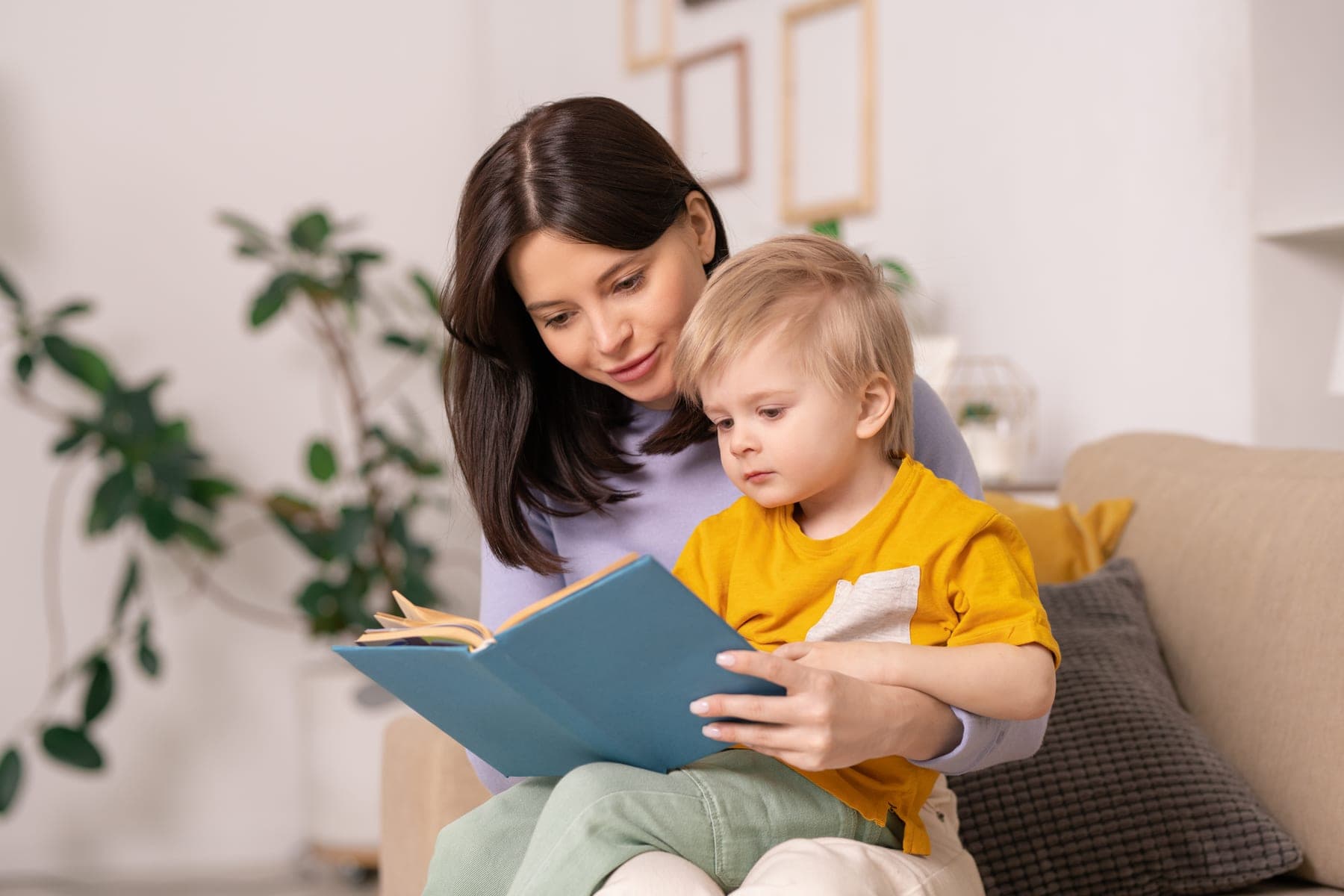 A mother reads a picture book with her toddler on the sofa