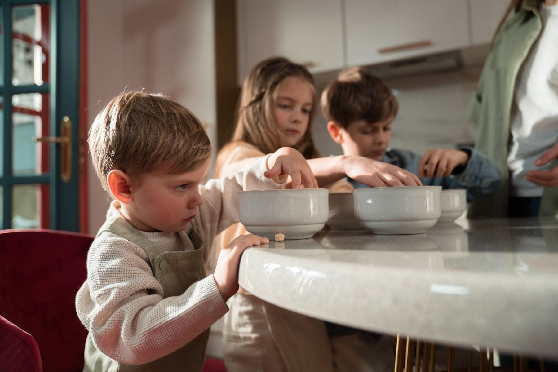 Three children gather around the breakfast table on a sunny morning