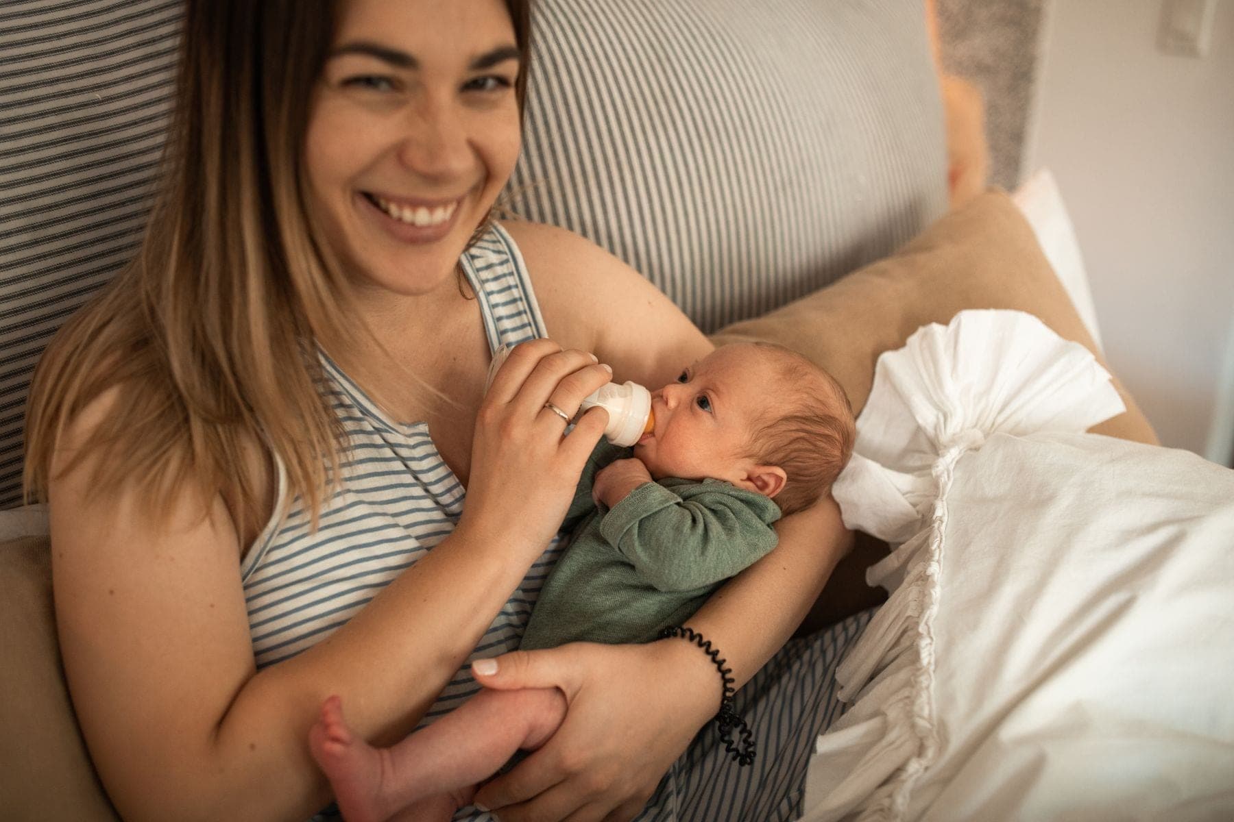 A smiling mother feeds her newborn with a bottle